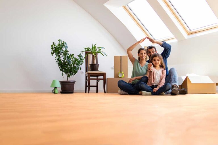 A couple reviews housing options on a laptop, surrounded by moving boxes and home decor samples.